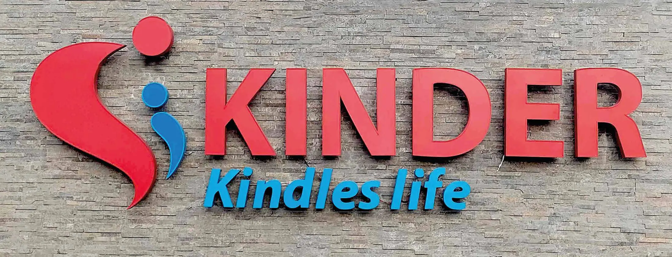 Kinder 3D lettering in red and blue on a stone-clad wall