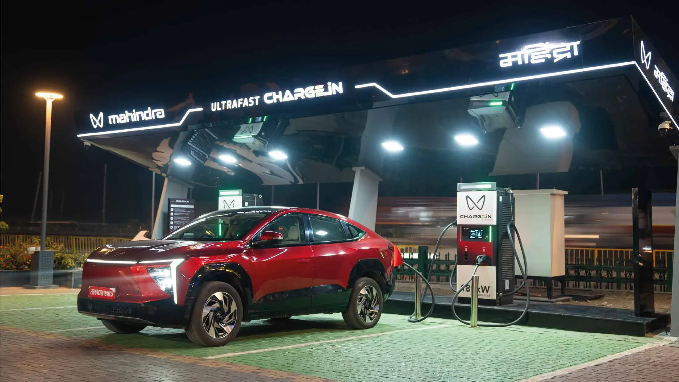 Mahindra Electric ultrafast charging station at night, with illuminated canopy branding and branded chargers